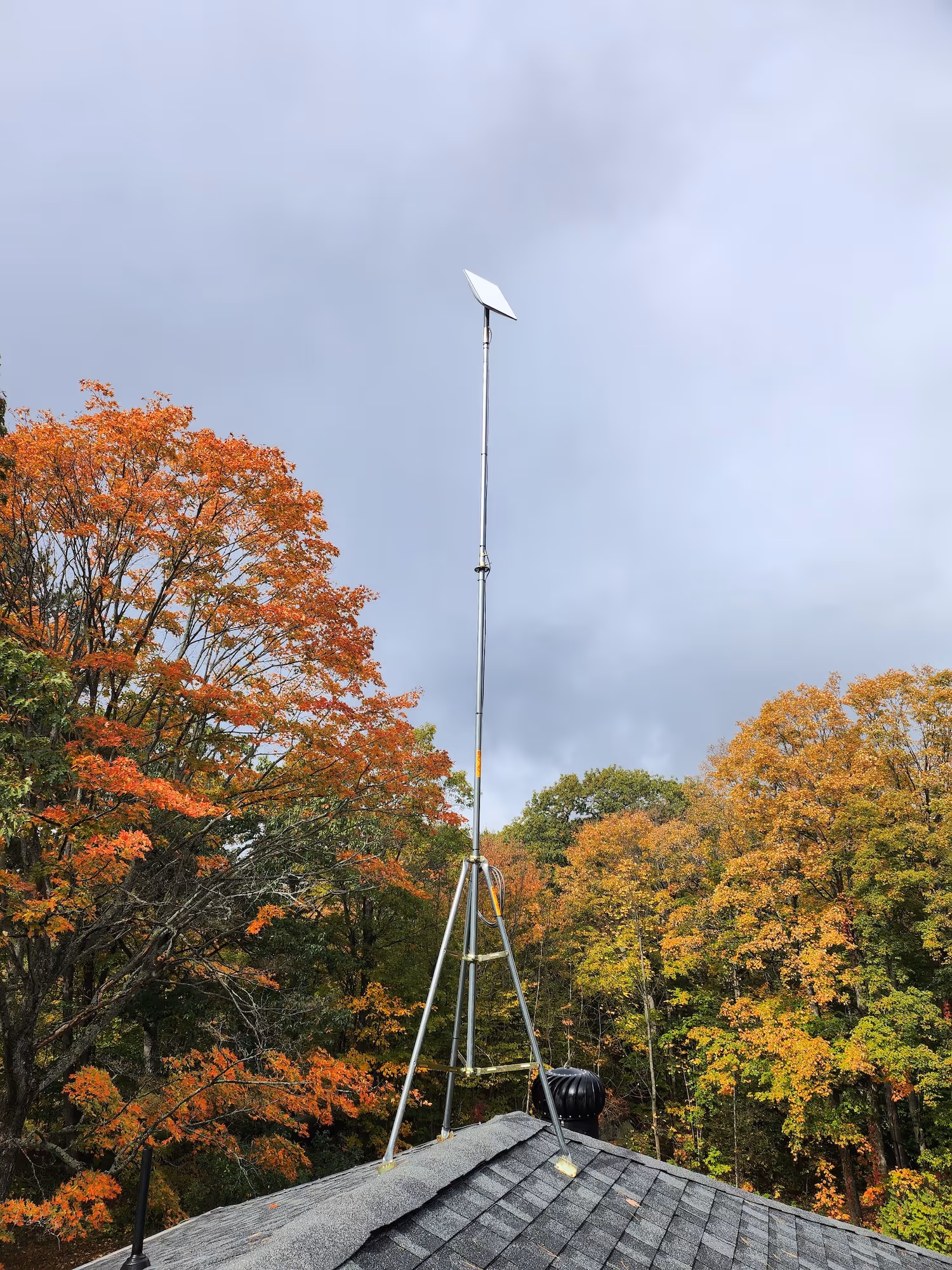 15 foot starlink tower on a rooftop tripod reaching above fall foliage